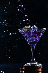 a cocktail glass with a drink inside stands on a stand with a slice of lime on the edge. neon trail behind the shot glass