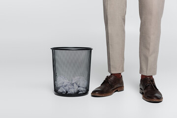 partial view of critic standing near trash can with crumpled paper on grey.