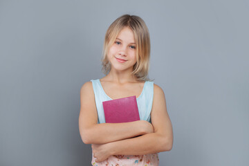 Happy school girl holding book and smiling on gray studio wall background