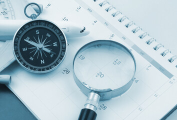 Airplane model with compass and magnifying glass on calendar page close-up. 