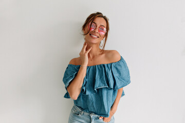 Smiling attractive woman in sunglasses touching her chin and looking aside over isolated background. Indoor portrait of european tanned woman 