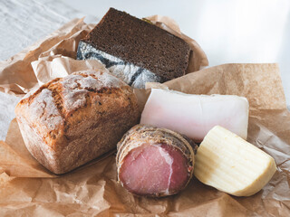 Delicious regional products on the craft paper. Wheat and rye bread, cheese and meat - obrazy, fototapety, plakaty