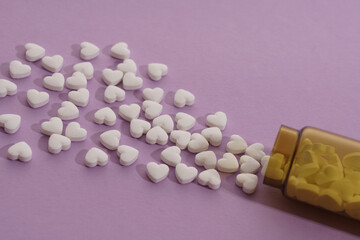 Top view of spilled heart shape pills on violet background with copy space