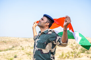 side view shot of happy indian army soldier holding waving Indian flag on top of mountian - concept national pride, nationalism, freedom and independence.