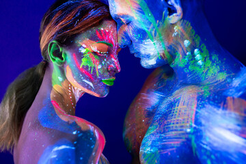 Portrait of a beefy man and woman painted in ultraviolet powder. Body art glowing in ultraviolet light