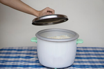 Hand opens lid of electric rice cooker after finish cooking for meal in the kitchen. Concept :...