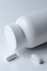 white plastic medicine jar and two white pills. light background