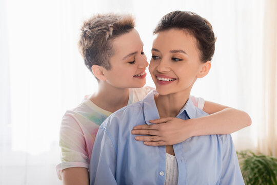 young bigender person with closed eyes embracing smiling partner.