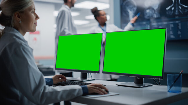 Hospital Research Lab: Female Medical Biotechnology Scientist Working on Green Screen Chroma Key Computer with Brain Scan MRI Images. Background: Neuroscientists Have Meeting Analysing MRI Scan