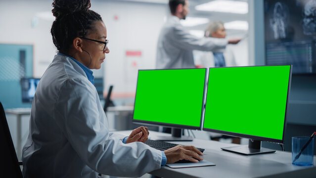 Hospital Research Lab: Black Female Medical Biotechnology Scientist Working on Green Screen Chroma Key Computer with Brain Scan MRI Images. Background: Neuroscientists Have Meeting Analysing MRI Scan