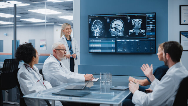 Hospital Conference Meeting Room: Neurologist Shows MRI scan, Magnetic Resonance Image on TV Screen, Team of Neuroscientists, Doctors Discuss Patient Treatment, Drug Research, Medicine Development