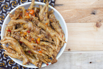 South African township delicacy, cooked chicken feet or walkie talkies with onion and sauce. flat lay on rustic wood with traditional South African printed Shwe Shwe cloth