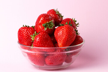 ripe appetizing strawberries in a transparent bowl close-up on a pink background