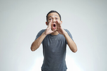 Close up portrait of a young asian man shouting loud with arm at his face isolated on studio...