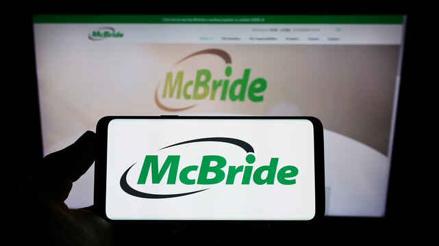 Stuttgart, Germany - 05-15-2022: Person holding mobile phone with logo of British household goods company McBride plc on screen in front of website. Focus on phone display.