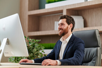 Smiling friendly relaxed businessman in the office seated at his desk behind a desktop monitor