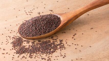 closeup of dry brown mustard seeds in a wooden spoon, small round healthy spice, herbal product taken on a wooden table top surface, copy space - obrazy, fototapety, plakaty