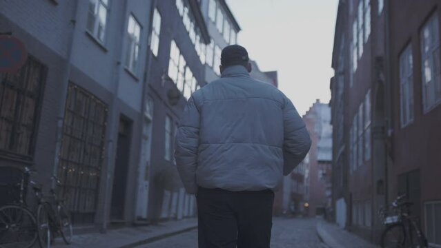 Guy in copenhagen in white jacket, walking down small city street. 60fps