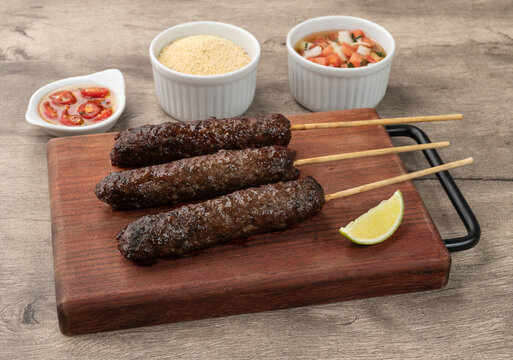 Meat Kafta skewers over wooden board with farofa and vinaigrette