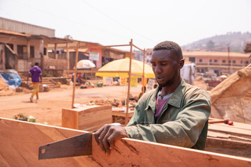 African carpenter in his open-air workshop sawing a board. Tiring handcraft