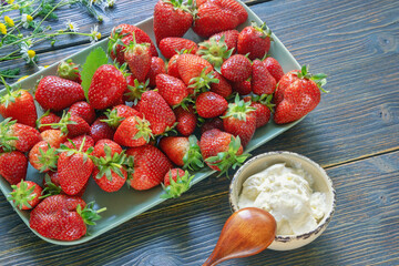 Plate with fresh strawberry and cup with sour cream on rustic table. Copy space