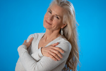 Portrait of happy smiling mature woman crossing arms isolated on blue background studio eyes toward product sale. People lifestyle concept