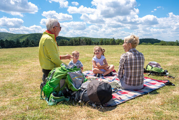 Grandparents and grandchildren having picnic while spending time together in the nature - obrazy, fototapety, plakaty