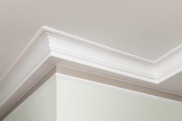 Angular ceiling skirting made of classic white crown moldings. Close-up detail of decoration in interior renovation. - obrazy, fototapety, plakaty