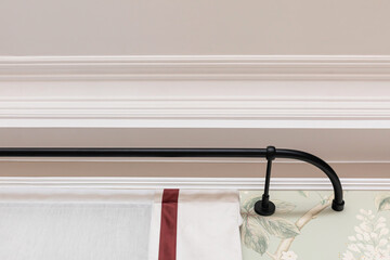 Ceiling skirting made of classic white crown moldings and bended curtain rod above window. Close-up detail of decoration in interior renovation.