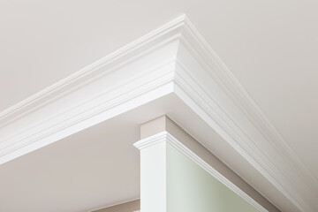 Angular ceiling skirting made of classic white crown moldings. Close-up detail of decoration in...
