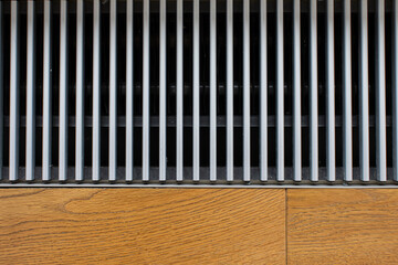 Floor-mounted metal grill of a modern convector heating built into the floor next to the window.
