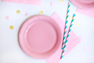 Pink paper disposable plate, napkin and straws for drinks on white background with confetti. Table setting for picnic. Bright eco-court. Birthday, party and holiday concept. Top view, flat lay