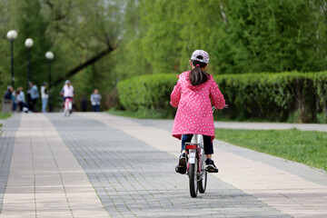 Kid girl riding on a bicycle on a path in a green park. Child cyclist, spring or summer leisure