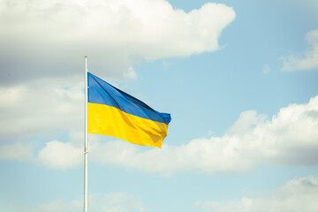 The big yellow and blue Ukrainian flag is waving in the wind as a symbol of independence and strength. Blue sky with white clouds in the background