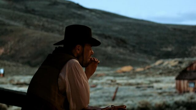 Portrait of cowboy enjoying the view from terrace of his house after hard day, smoking a cigar. Spaghetti, macaroni western style cinematic footage
