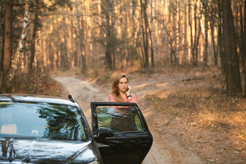 confused young woman standing next to the car with opened door and talking on the phone