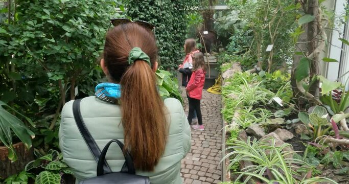 Family at botanical garden. Mother taking photo of daughters in greenhouse. Tropical green exotic plants.
