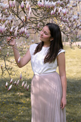 A young girl in delicate magnolia flowers. Spring in the park. Youth and teenagers