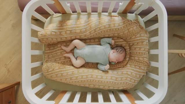 Little baby lies in crib and falls asleep at home during daytime. Female infant resting in bed, top view