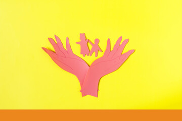 Cardboard figures hold small children with open palms. The concept of family and child protection