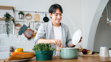 Smiling Asian handsome man cooking in kitchen at home.Young Asian male Chef cooking romantic dinner at home taste soup.