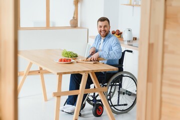 Young Disabled Man Sitting On Wheel Chair Preparing Food In Kitchen