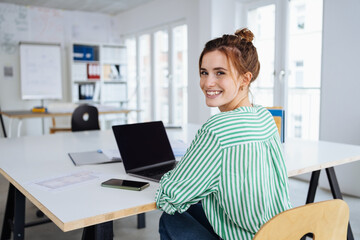 Young businesswoman sitting in office in front of laptop looking at camera