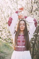 young beautiful Ukrainian woman in vyshyvanka  - ukrainian national clothes. Woman in countryside near the blossoming tree.  Stand with Ukraine  