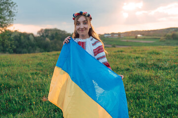 portrait of young Ukrainian woman in vyshyvanka  - ukrainian national clothes. She is holding ukrainian flag - symbol of freedom and independence. Stand with Ukraine
