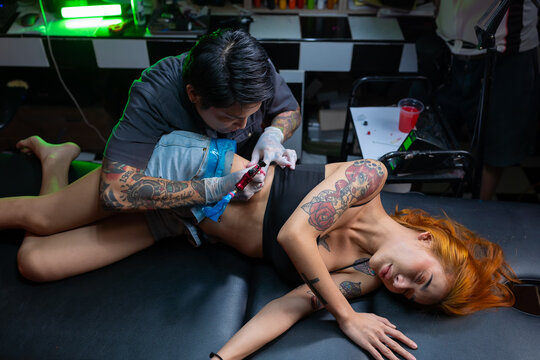 Tattoo artist professional stuffing a tattoo on a female body under the lamp light. Tattoo artist in a studio.