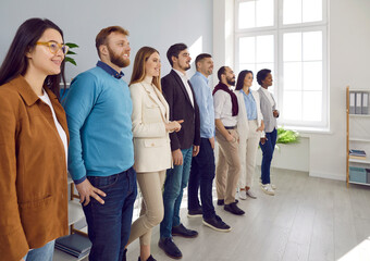 Diverse team of successful business people standing all together in their office. Group of happy confident young men and women standing in a row, looking away and smiling