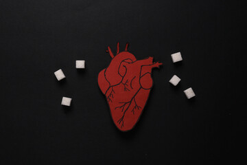The harm of sugar on the heart. sugar cubes with anatomical heart on black background