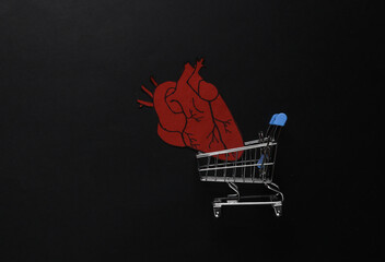 Heart implantation concept. Shopping cart with an anatomical heart on black background....