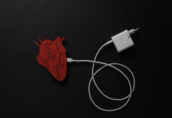 Charge your heart. Anatomical heart with charger cable on black background. Energy charge.